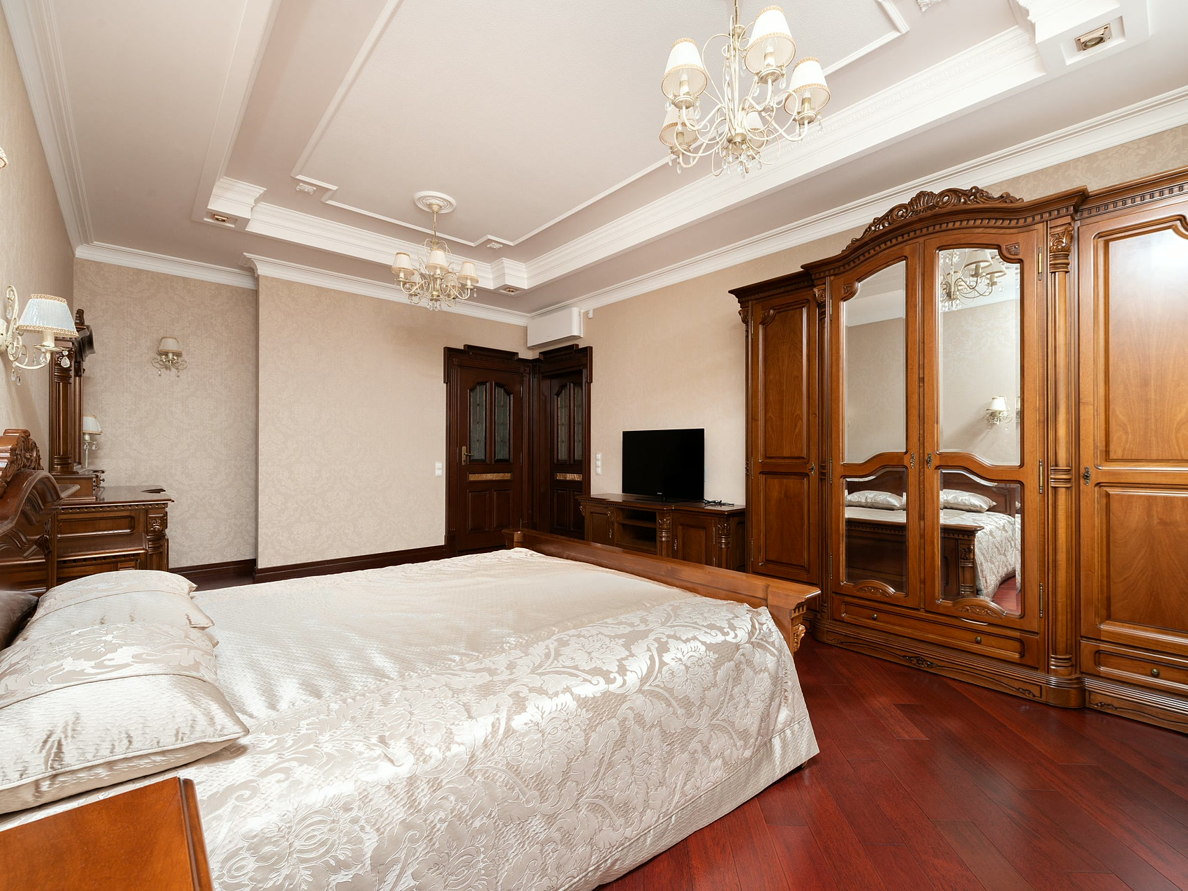 Bed with white linen beside wooden cabinets under an ornate ceiling